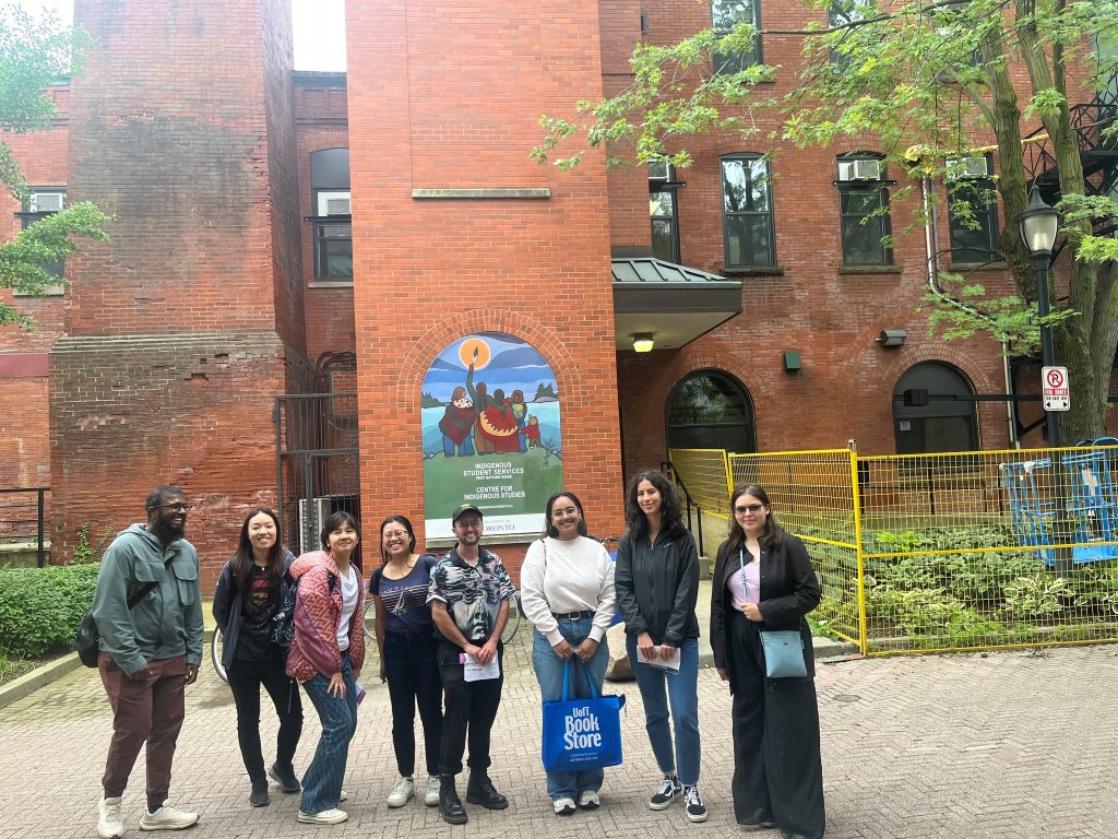 A group of grad students smiling and standing in front First Nations House.