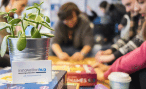 Innovation Hub business card propped up by small jade plant with students in background