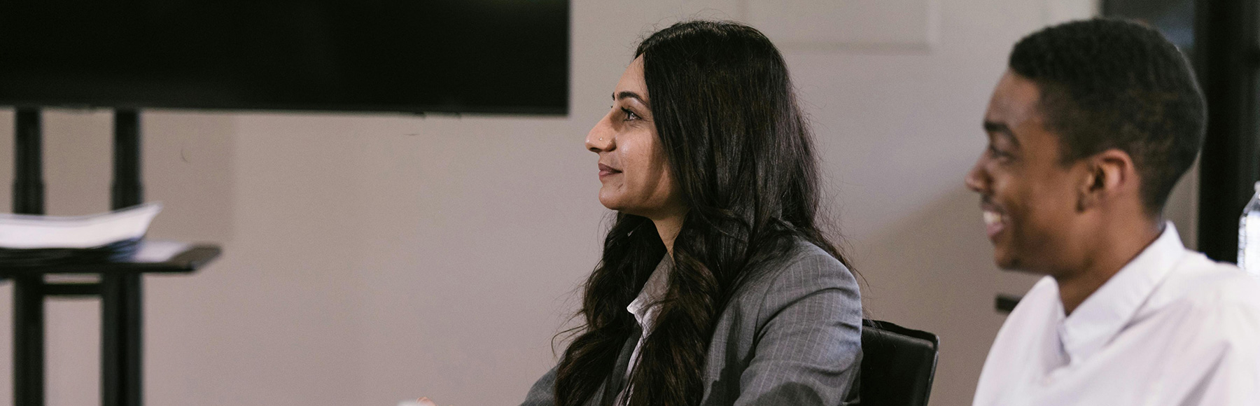 Two people sit in a classroom style environment looking off to the front of the room.