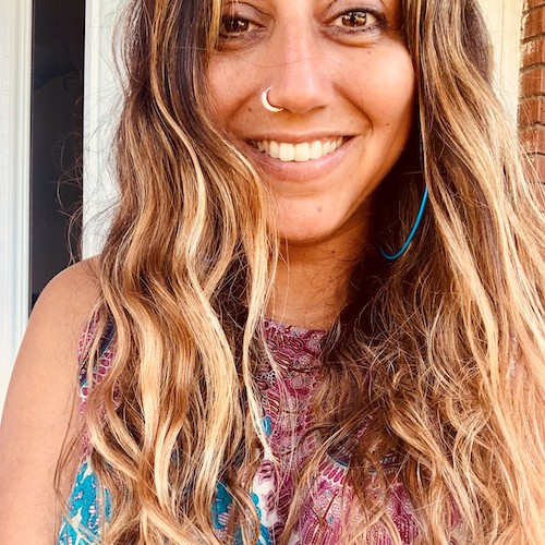 Reshma Dhrodia smiles in a selfie. Her hair is highlighted with blonde and wavy. She wears a silver nose ring.