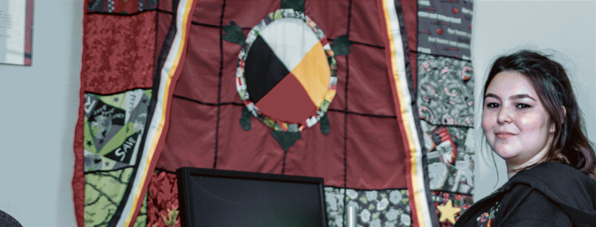 Indigenous student sitting at computer with wall quilt in background