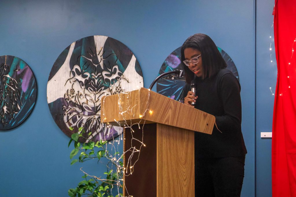 Catherine standing behind the podium and holding the microphone as she performs her piece.