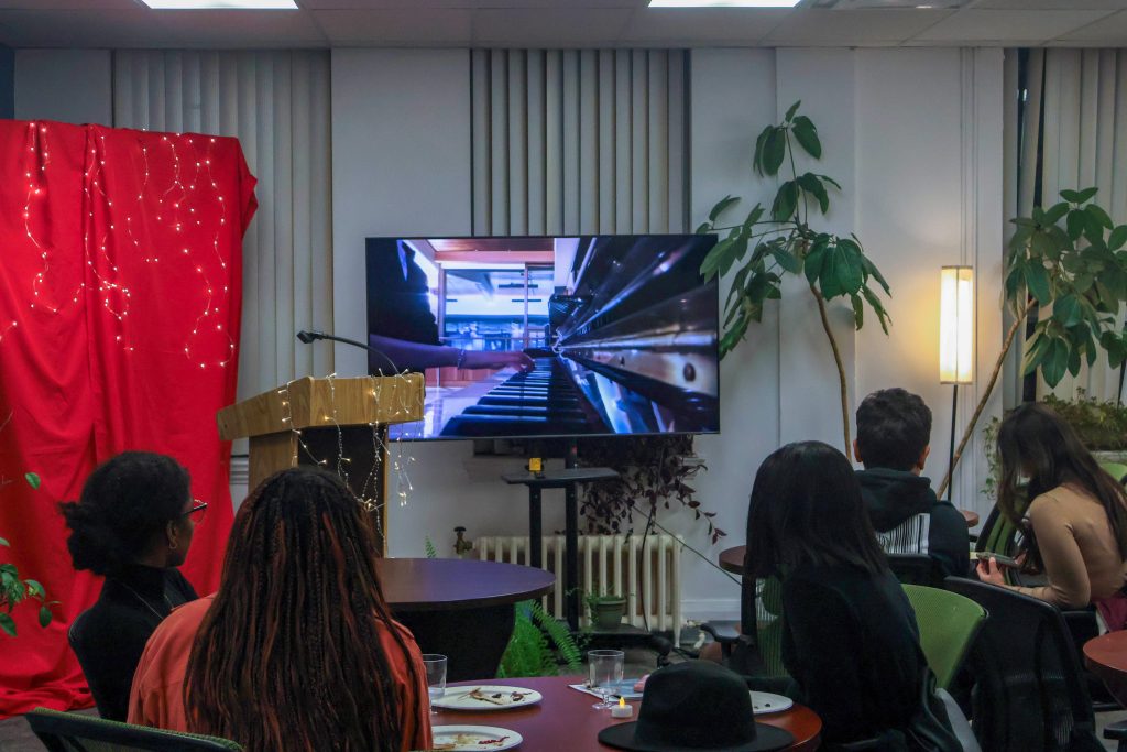 Students sitting in the audience, watching a recorded piano performance.