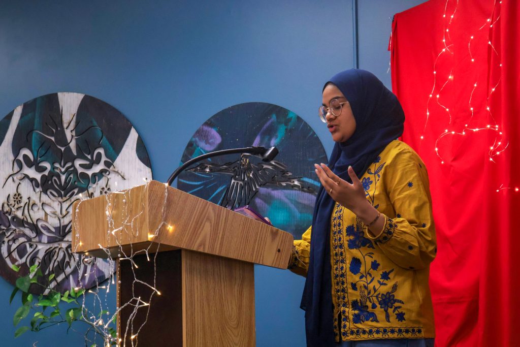 A student raising their hands up as they read their piece standing behind the podium.