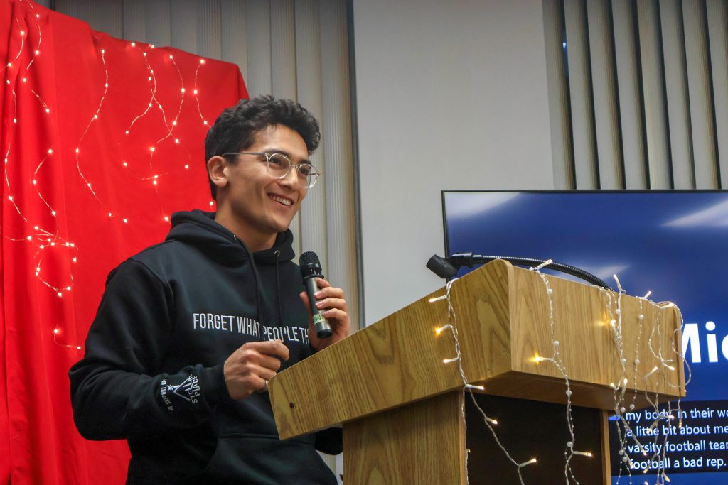 A student holding the microphone and smiling behind the podium as they perform their piece.