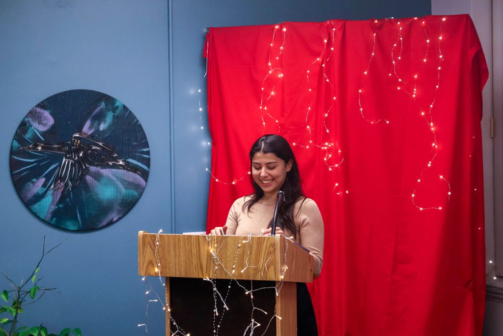 A student smiling while reading their piece and standing behind the podium.