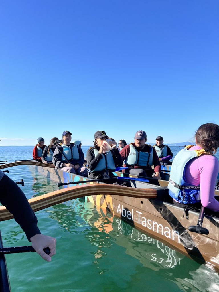 Students resting from paddling a Waka canoe while one student blows the Conch Shell.