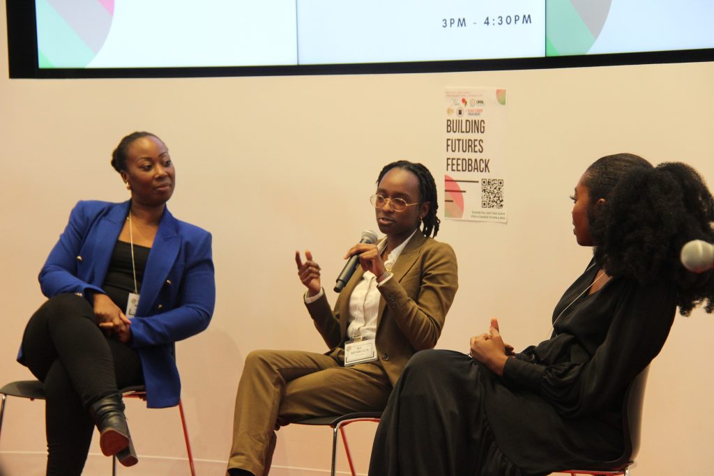 Panel of 3 speakers sitting at the front of the room while one panelist speaks into a mic.