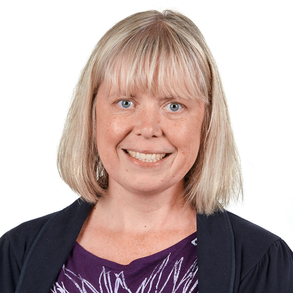 Heather Kelly smiles toward the camera in front a white background. She has a blonde bob with bangs and has blue eyes.