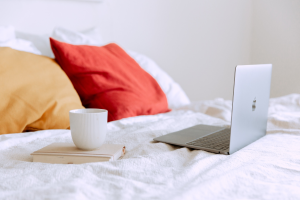 Laptop and cup of tea on bed with throw pillows