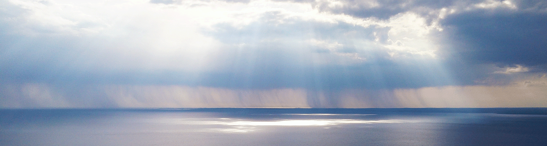 Cloudy sky with light streaming through to touch water