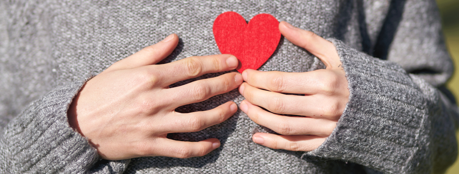 Hands holding a felt cutout heart agains a grey sweater