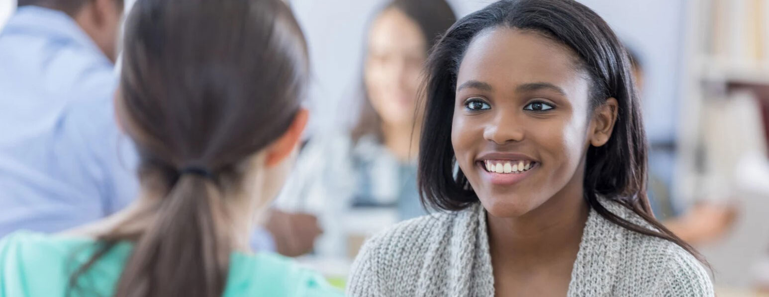 Two people talking, facing each other with one person facing the camera and the other with the back of their head to the camera.