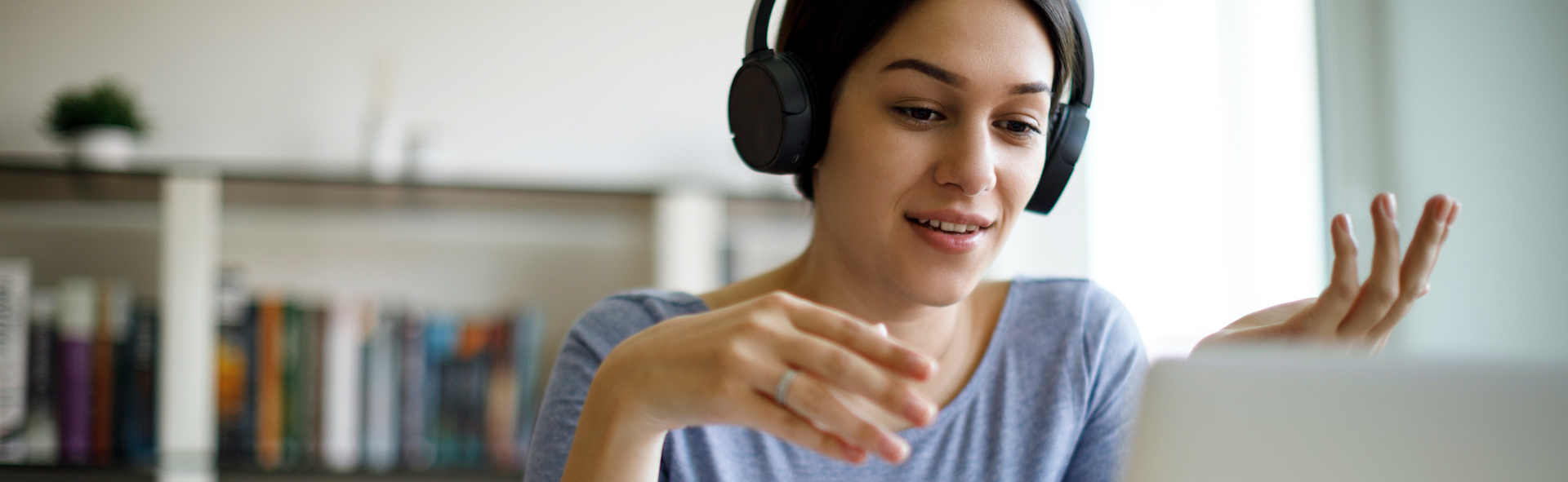 A person sits at a desk with headphones on and looks into a computer screen on a video call