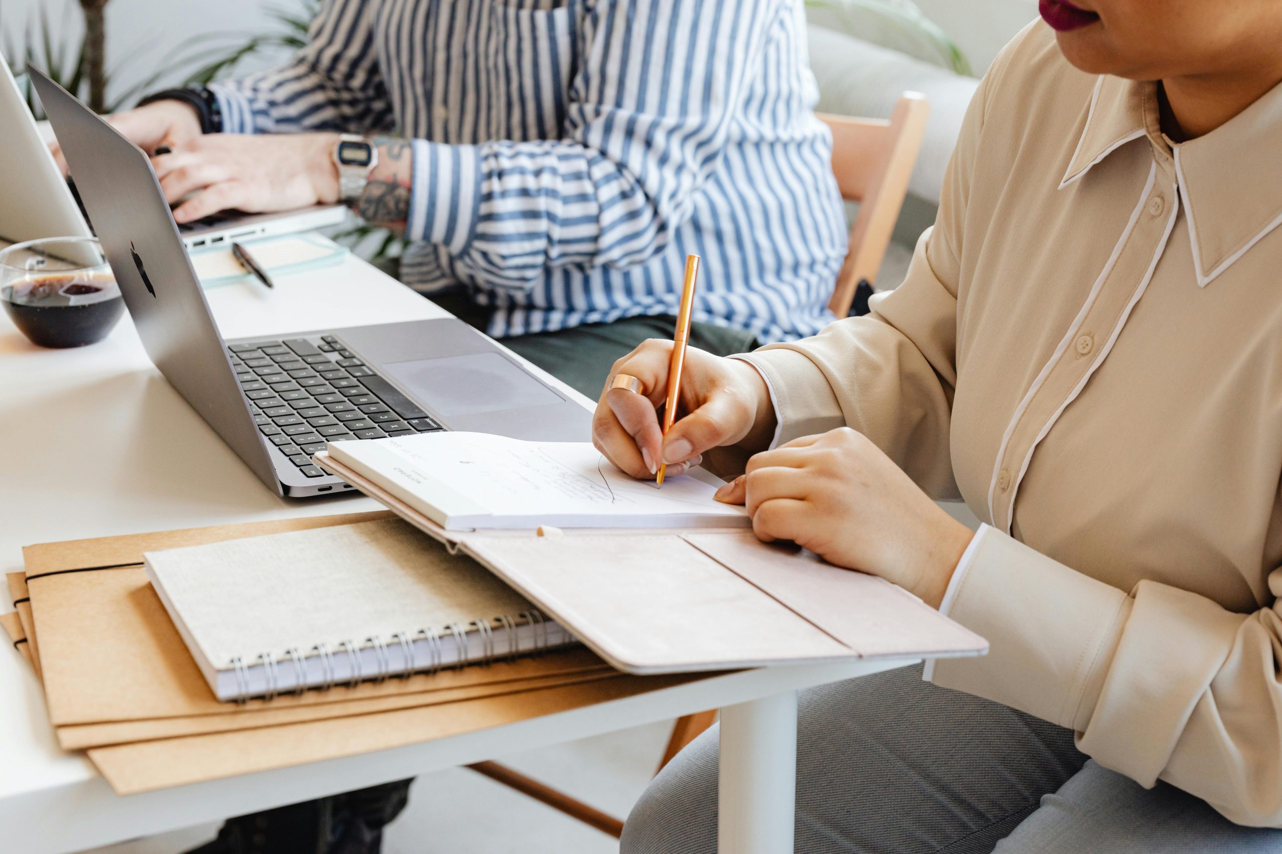 Two people sitting and working side by side with notebooks and computers.