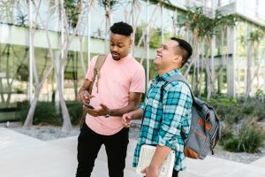 Two male students laughing in front of glass building with palm trees