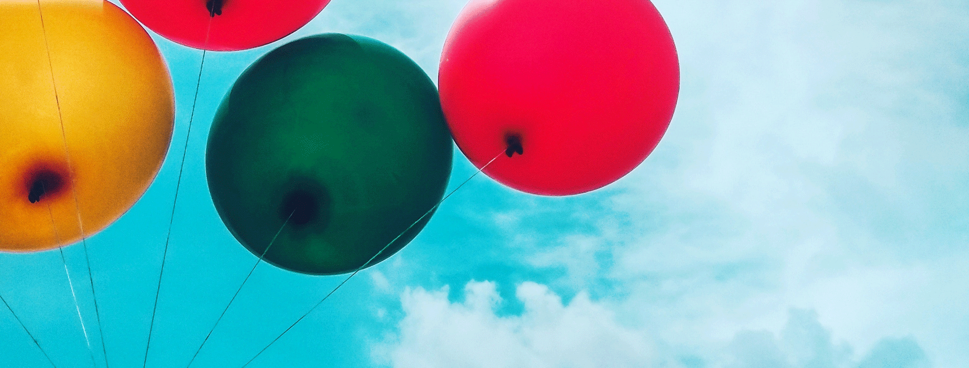 Four multi-color balloons against a blue sky