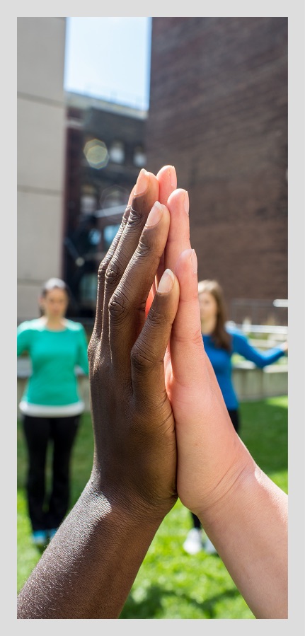 A black hand and a white hand pressing palms together as part of a yoga circle