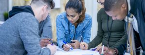Group of students writing around a chart paper and talking.