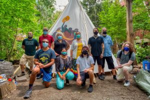 Tipi raising attendees kneeling and standing in front of tipi, wearing masks.