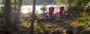 Two red muskoka chairs beside lake