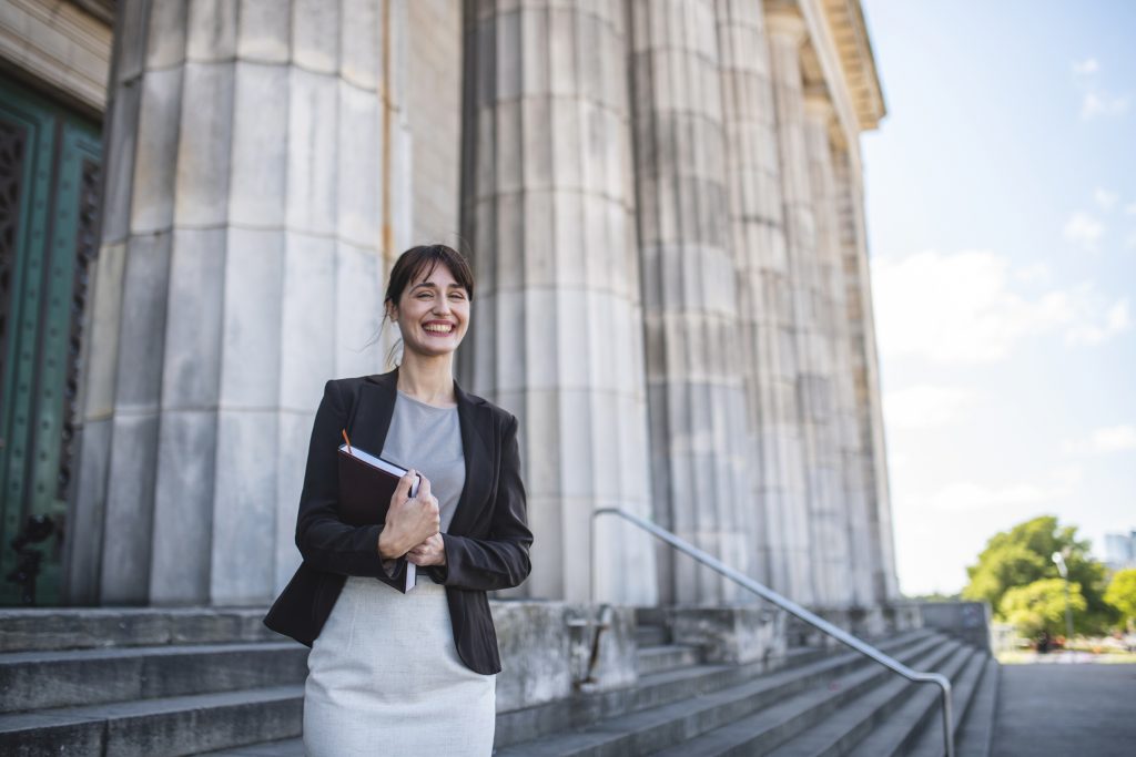 Mid-adult female law student in business attire smiling outside university building