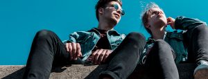 Two young people sitting on a stone against a blue sky