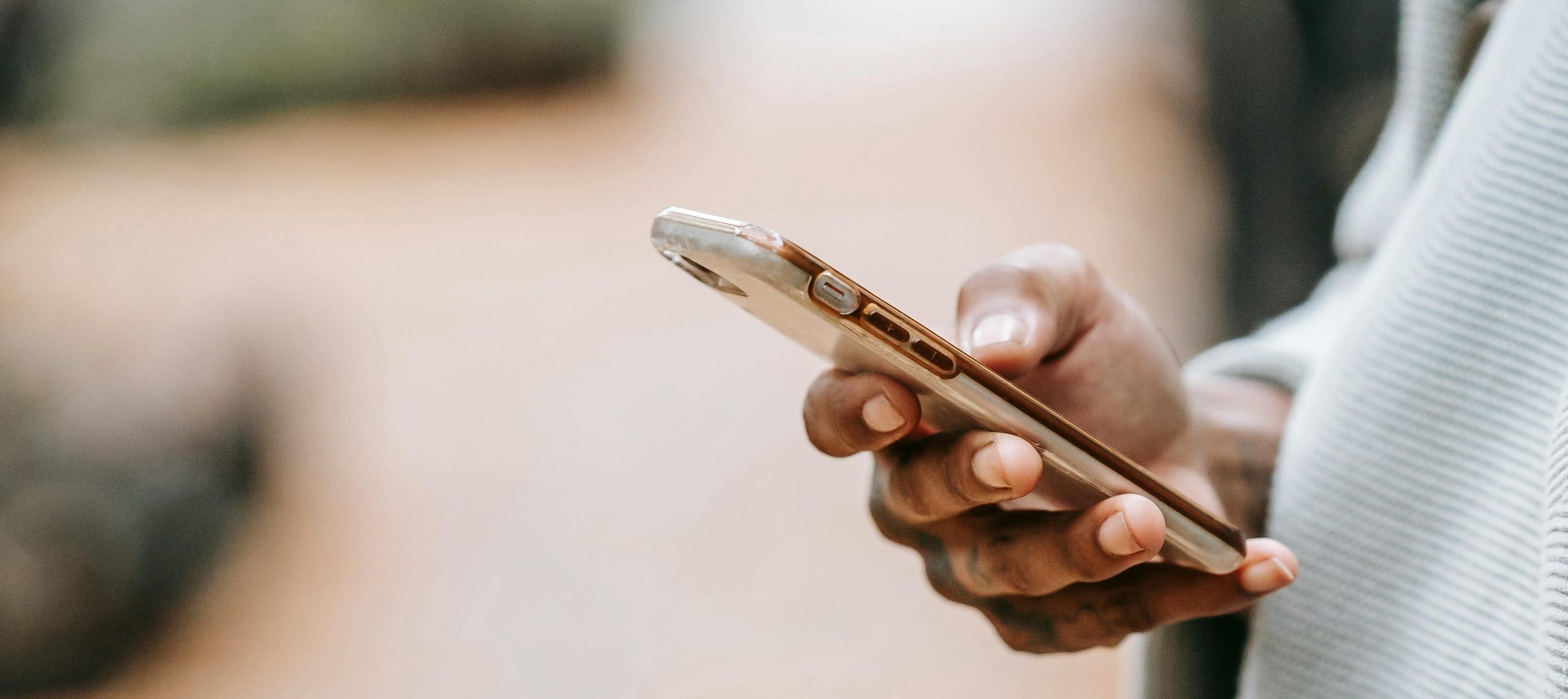 A person's hand holding a phone outside. The person's thumb is scrolling the phone.