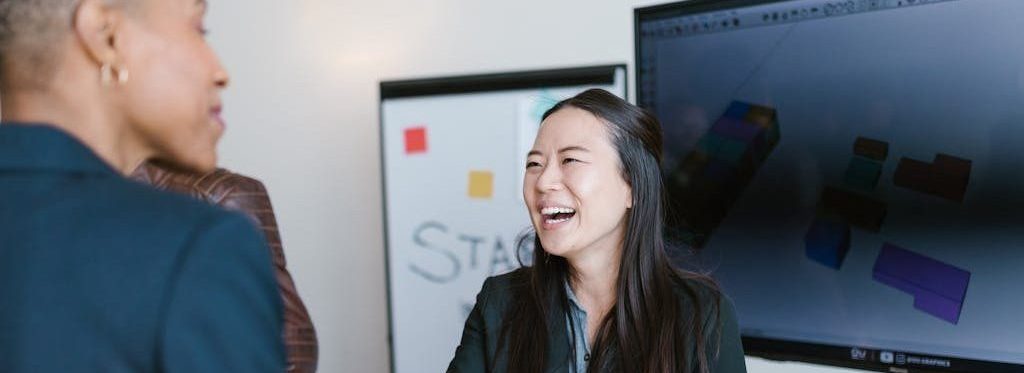 Woman in blazer smiling and shaking another woman's hand.